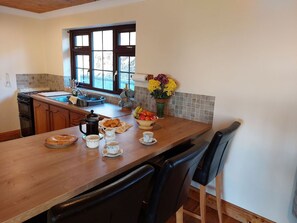Una cocina con una mesa de madera, sillas, cafetera y frutero.