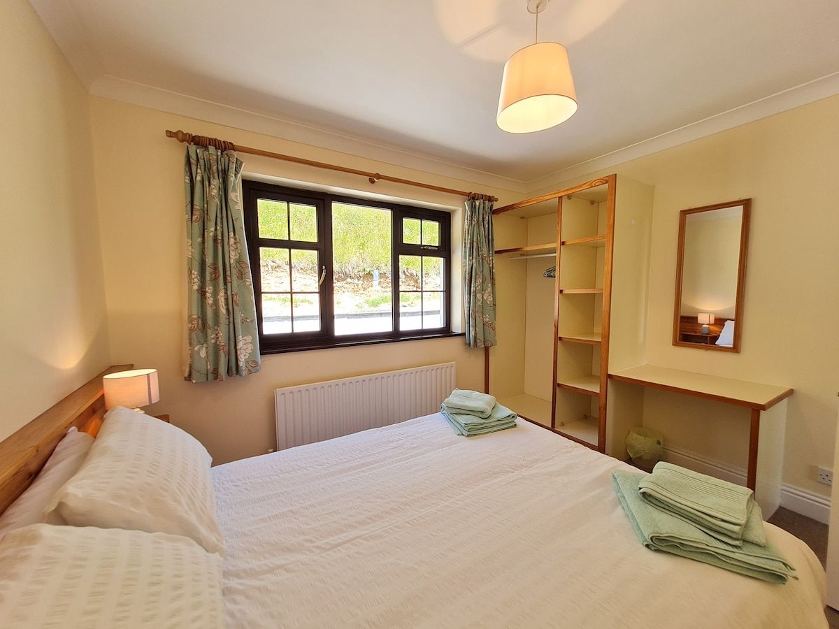 Une chambre à coucher avec un lit, une fenêtre avec des rideaux, un radiateur, une armoire et un miroir.