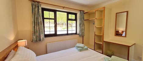 A bedroom with a bed, a window with curtains, a radiator, a wardrobe, and a mirror.