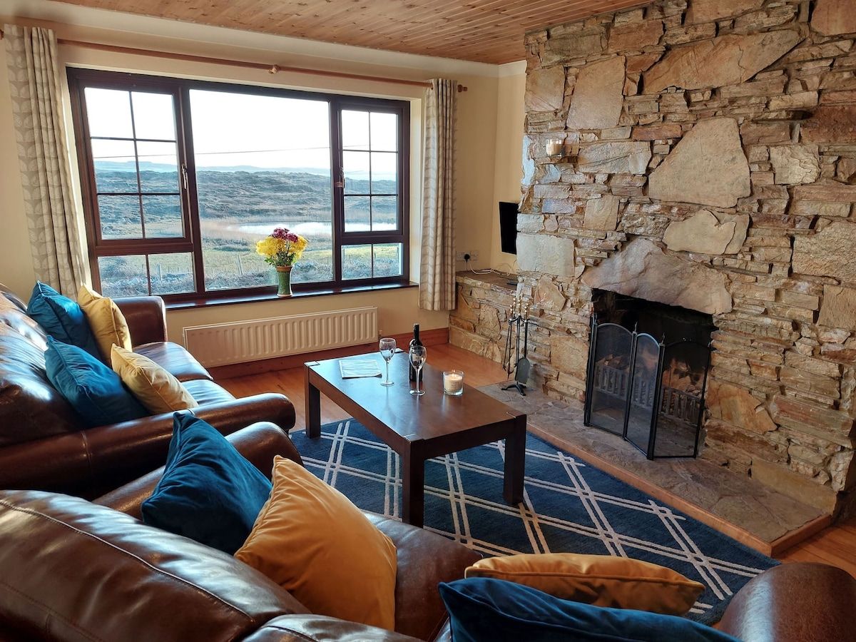 A cozy living room with a stone fireplace, leather sofa, and a view of the outdoors.