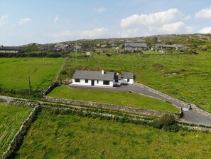 Una casa blanca con techo gris, rodeada por un muro de piedra y un campo cubierto de césped.