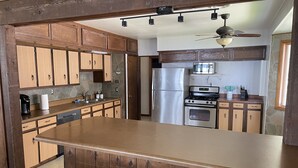A kitchen with wooden cabinets, a stainless steel refrigerator, an oven, and a bar stool area. - Lakefront home with 3 bedrooms, 2 baths, great for groups up to 10 (Shelbyville)