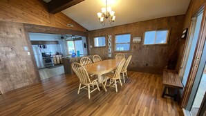 A wooden interior with a dining table surrounded by chairs, a kitchen in the background, and a sign reading "GATHER HERE". - Lakefront home with 3 bedrooms, 2 baths, great for groups up to 10 (Shelbyville)