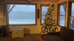 A cozy cabin interior with a large window overlooking a snowy landscape, a decorated Christmas tree, and a wooden ceiling. - Lakefront home with 3 bedrooms, 2 baths, great for groups up to 10 (Shelbyville)