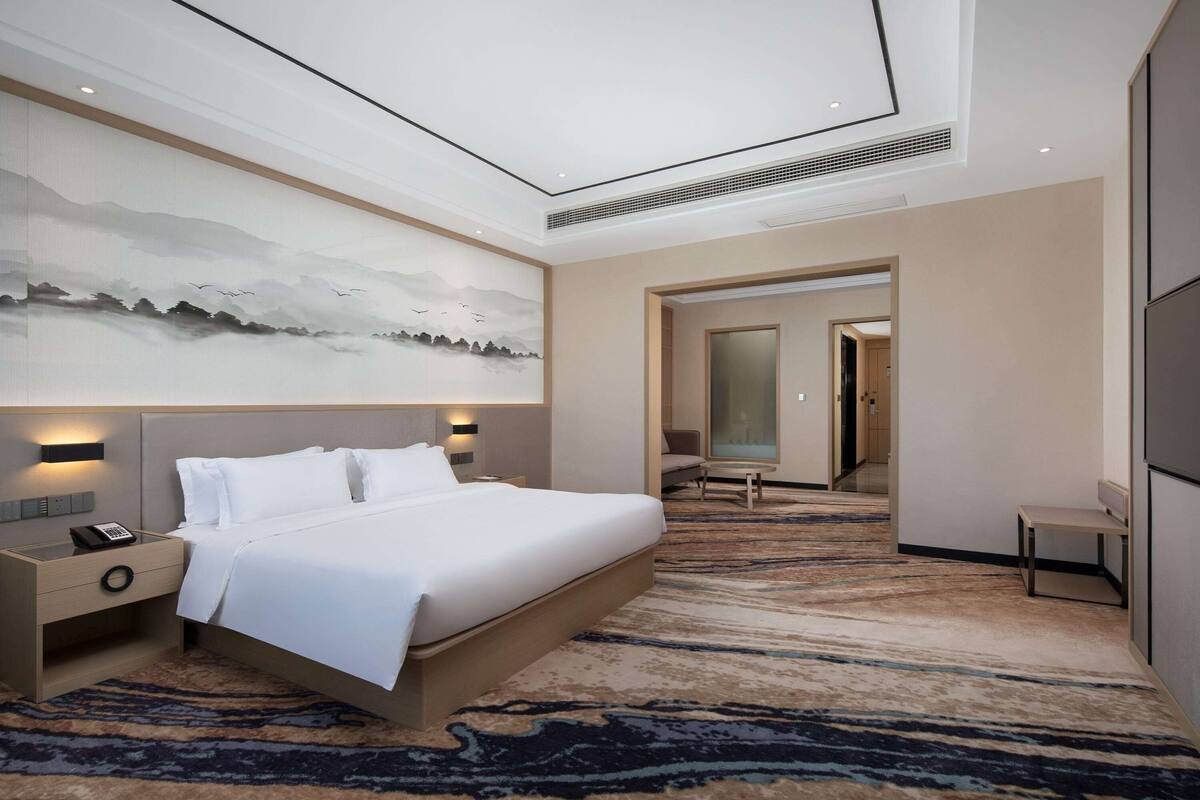 A hotel room with a large bed, bedside tables, a wall-mounted phone, and a carpeted floor.