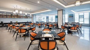 Un comedor amplio con varias mesas y sillas, luminarias modernas y vistas de la ciudad a través de amplias ventanas.
