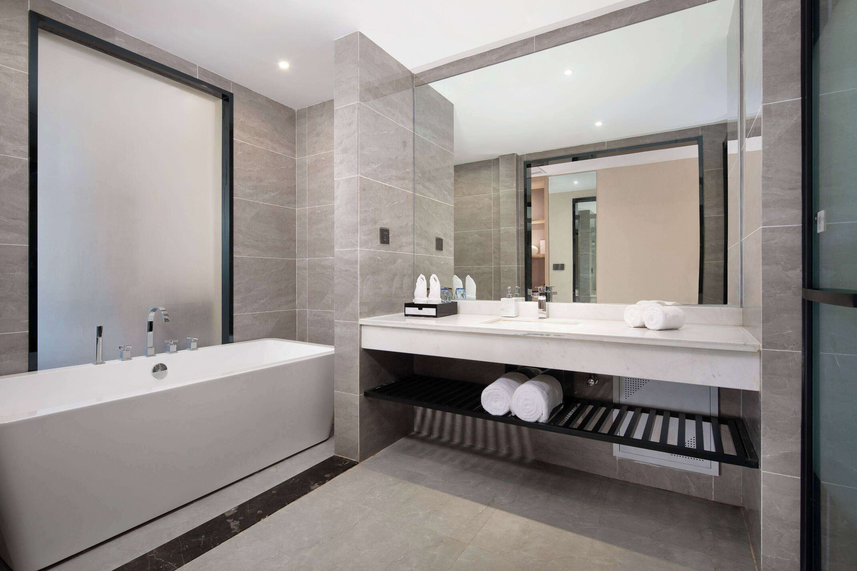 A modern bathroom with a large bathtub, a vanity with a mirror, and a towel rack.
