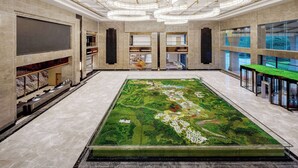 Un vestíbulo espacioso con un amplio paisaje artificial de color verde, suelo de mármol y modernos candelabros.