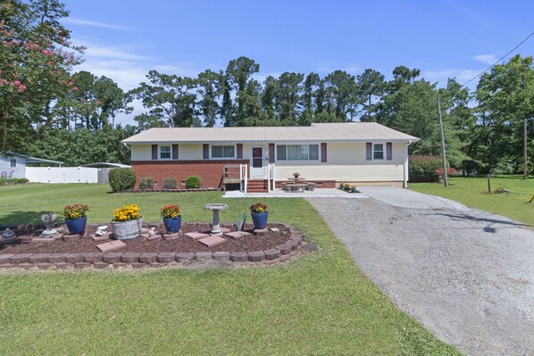 A single-story house with a front porch, a small garden with potted plants, and a gravel driveway.