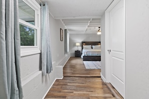 A narrow hallway with wooden flooring leading to a bedroom with a bed and a nightstand.