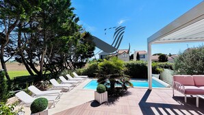 Un área junto a la piscina con sillas de descanso, una piscina pequeña y una pérgola.