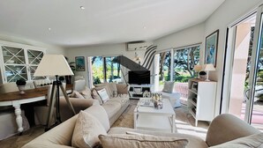 Amplia sala de estar con un sofá grande, una mesa de centro y un televisor. Hay un comedor con una mesa y sillas, y un balcón con vistas al exterior.