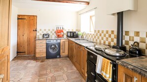 A compact kitchen with a washing machine, a microwave, and a stove. - Penrallt Fawr (Caernarfon)