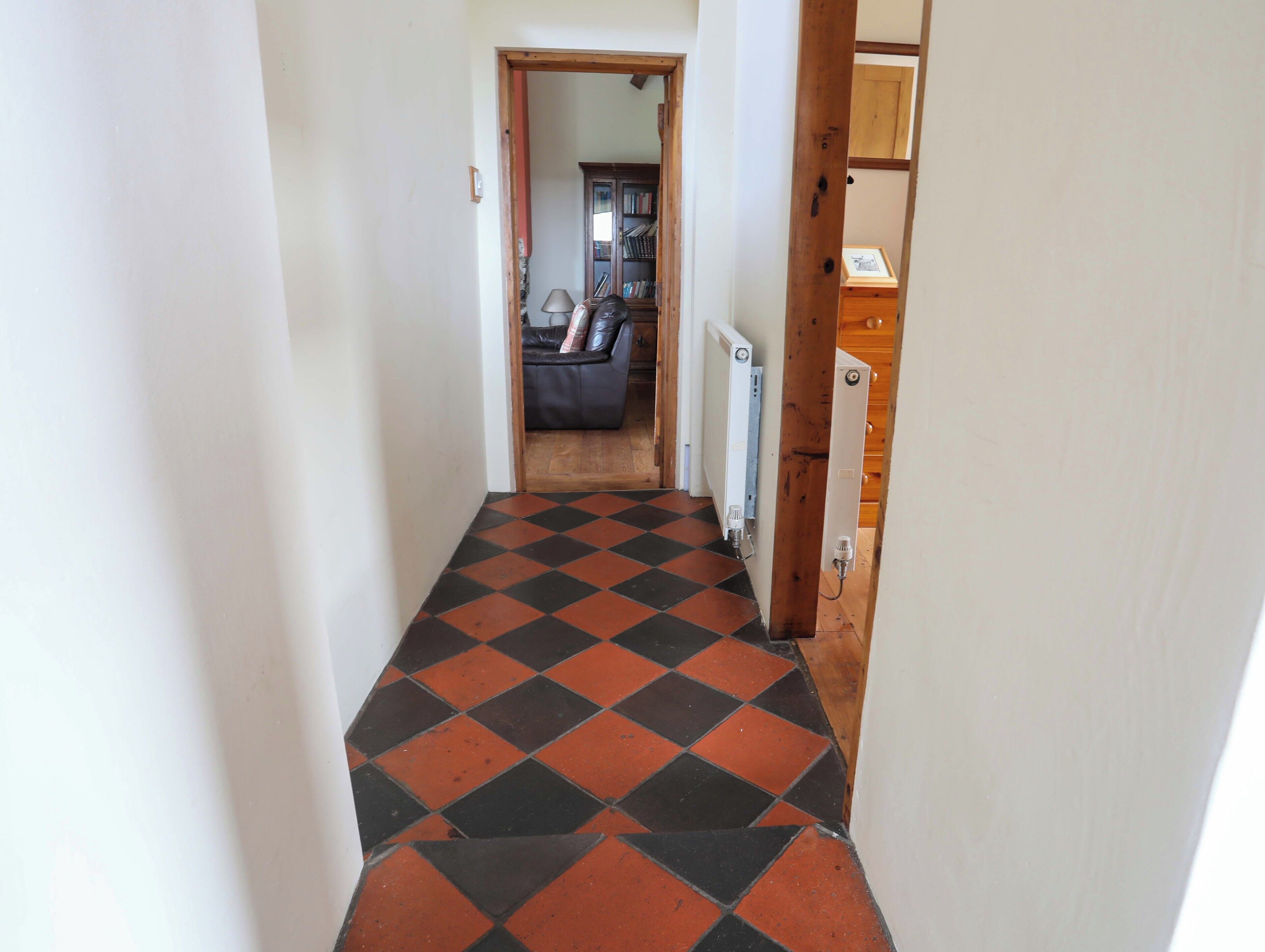 A narrow hallway with a checkered floor pattern, leading to a living area with a sofa and a cabinet.