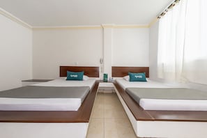A hotel room with two beds, each with a wooden headboard and a teal pillow. The room has white walls and a tiled floor. - Ayenda Parque del Quindio (Armenia)
