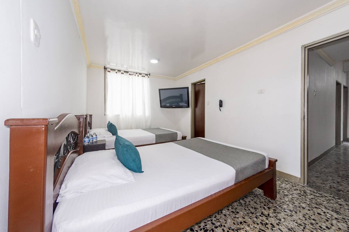 A hotel room with a single bed, a bedside table, a TV, and a door leading to a hallway.