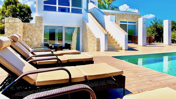 Une maison moderne à deux étages, dotée d’une piscine, d’un espace de détente extérieur et d’un mur en pierre.