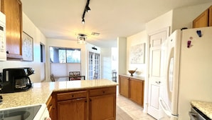 A kitchen with wooden cabinets, a white refrigerator, a coffee maker, and a dining area with a chair and table.
