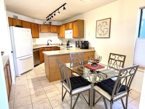 A modern kitchen with wooden cabinets, a white refrigerator, a coffee maker, and a dining table with chairs.