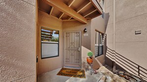 A residential entrance with a metal gate, a welcome mat, a potted plant, and a number sign.