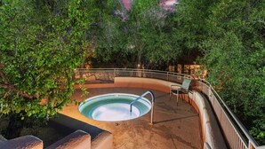 A hot tub surrounded by dense foliage, with a curved wooden deck and metal railing.