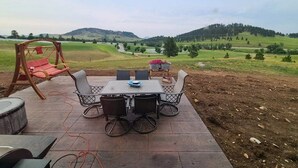 Un patio exterior con una mesa y sillas, un columpio y vistas de un paisaje verde con colinas.