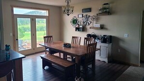 Un comedor con mesa y sillas de madera, una araña y vistas al exterior a través de un ventanal.