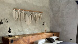 Une chambre moderne avec une tête de lit en bois, un lit avec une literie blanche et foncée, une table de chevet avec une lampe et des décorations murales en macramé.