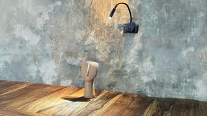 Une pièce au style rustique, avec un plancher en bois, un mur gris à la texture intéressante et un luminaire moderne.