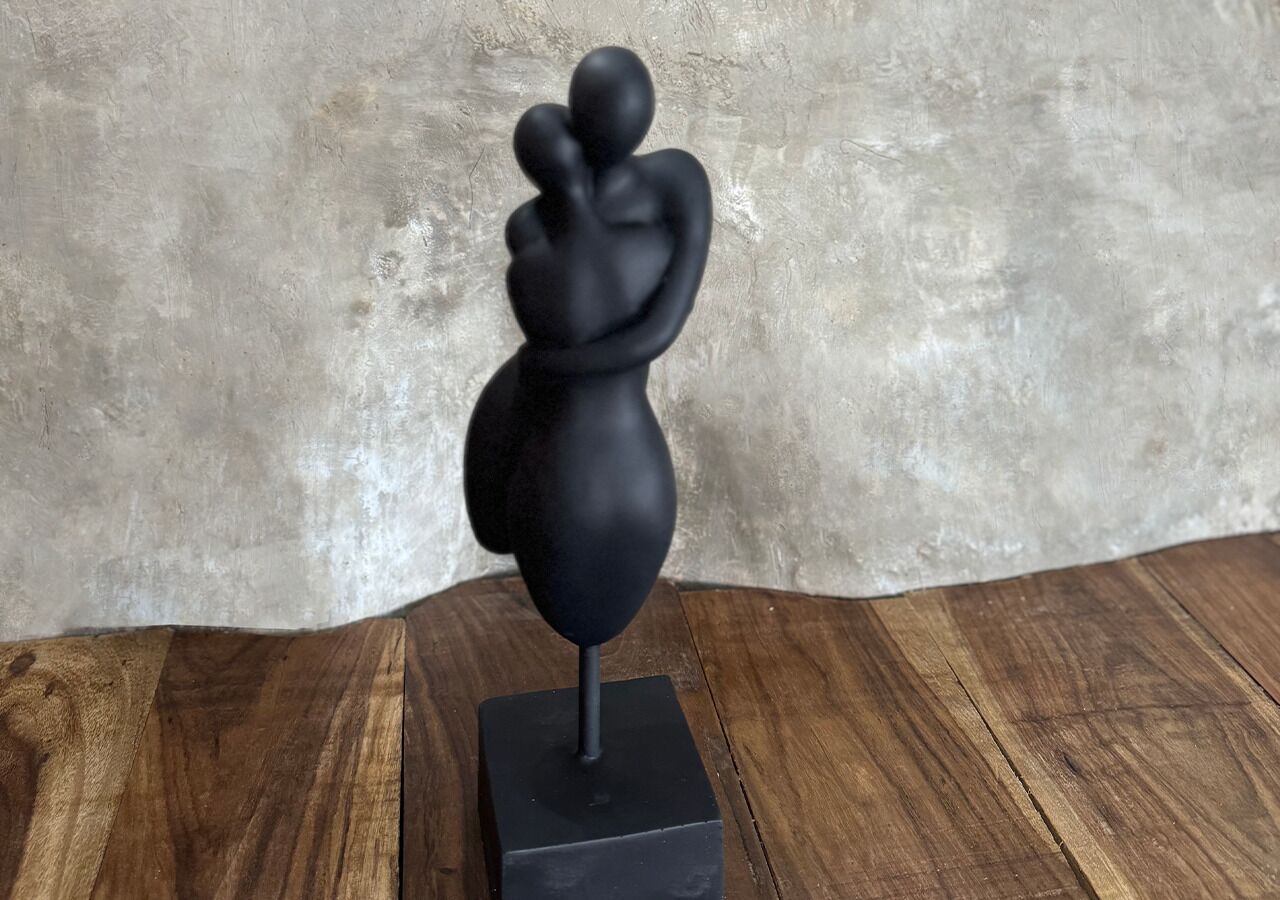 A sculpture on a wooden base against a textured wall.