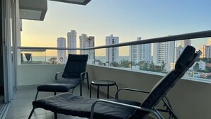 Ein Balkon mit zwei Liegestühlen und einem kleinen Tisch, mit Blick auf eine Skyline mit Hochhäusern.