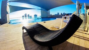 A sunlit outdoor area with a pool, lounge chairs, and a view of a city skyline. - Sea View Santa Marta  (Gaira)
