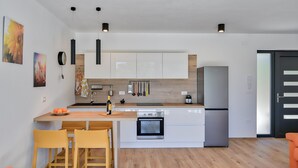Eine moderne Küche mit weißen Schränken, einem eingebauten Backofen und einem Kühlschrank. Holzstühle und ein kleiner Tisch sind ebenfalls vorhanden.