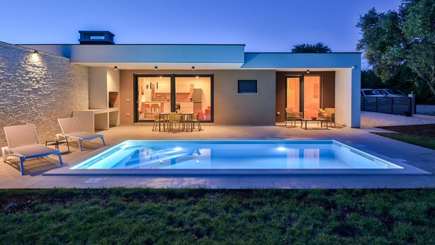 Ein modernes Haus mit Swimmingpool, Sitzgelegenheit im Freien und einem gut beleuchteten Innenraum.