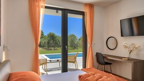 Ein Hotelzimmer mit einem Bett, einem Schreibtisch, einem Stuhl, einem Fernseher und Blick auf einen Pool.
