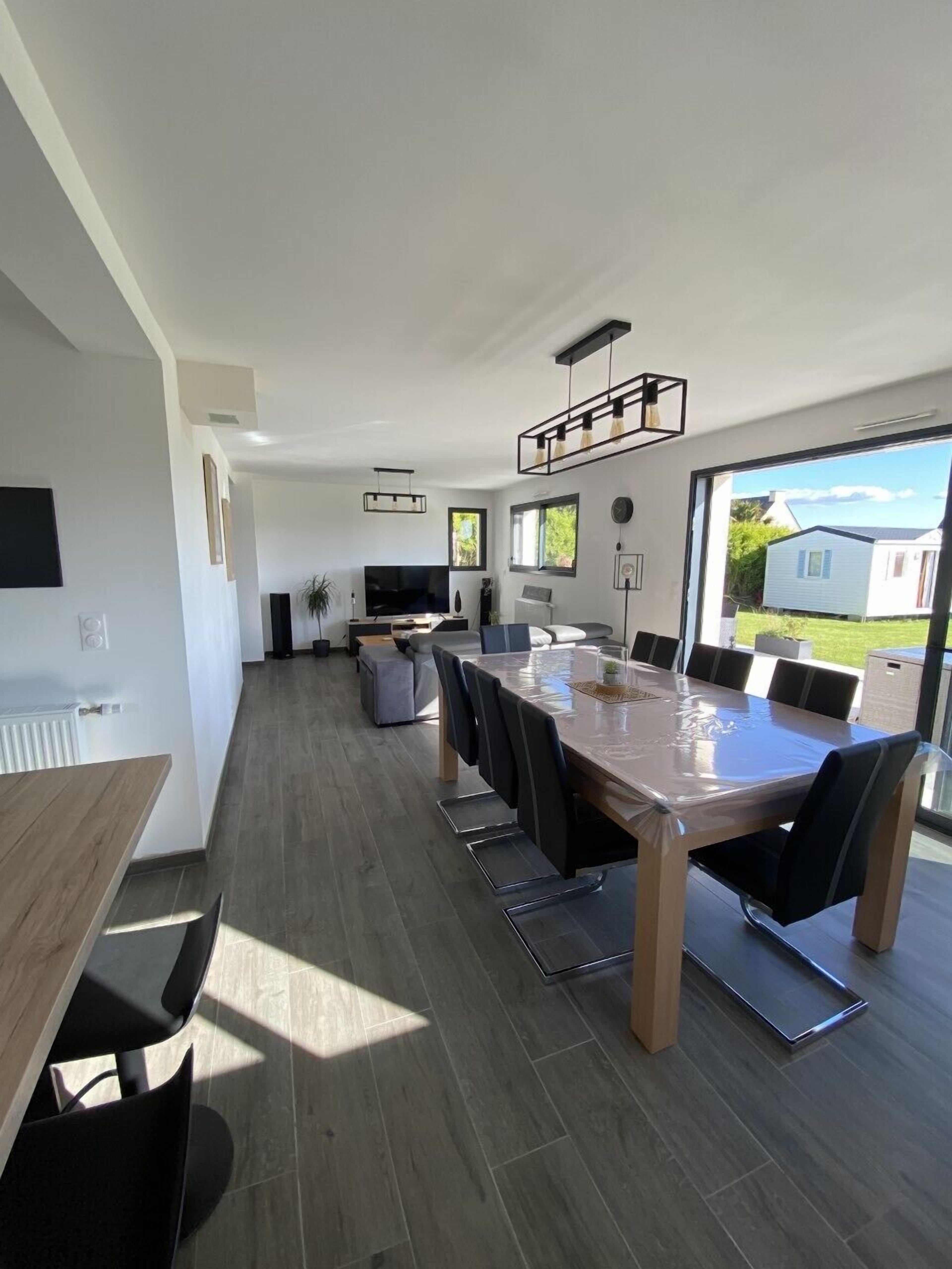 A modern kitchen with a large dining table, built-in appliances, and a view of the outdoors.