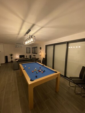 Una mesa de billar con bolas, un ventilador de techo y una zona de estar con sofá y sillones.