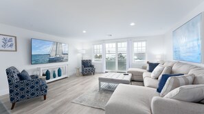 Uma sala de estar ampla, com uma grande janela, lareira e vista para o mar.