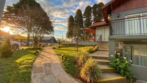 A residential property with a stone pathway leading to a wooden deck, surrounded by greenery and trees. - Pousada Ville Vie (Gramado)