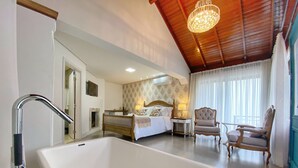 A spacious bedroom with a large white bathtub, a wooden ceiling, and a bed with a nightstand and lamps. - Pousada Ville Vie (Gramado)