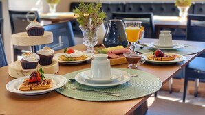 A breakfast setting with a three-tiered cake stand, plates of waffles, pastries, and a fruit bowl. - Pousada Ville Vie (Gramado)