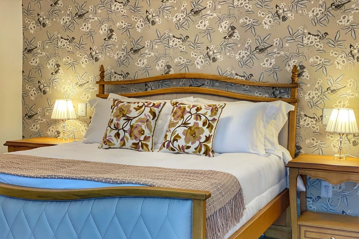 A bed with a wooden frame, floral-patterned pillows, and a quilted headboard. There are two bedside tables with lamps.