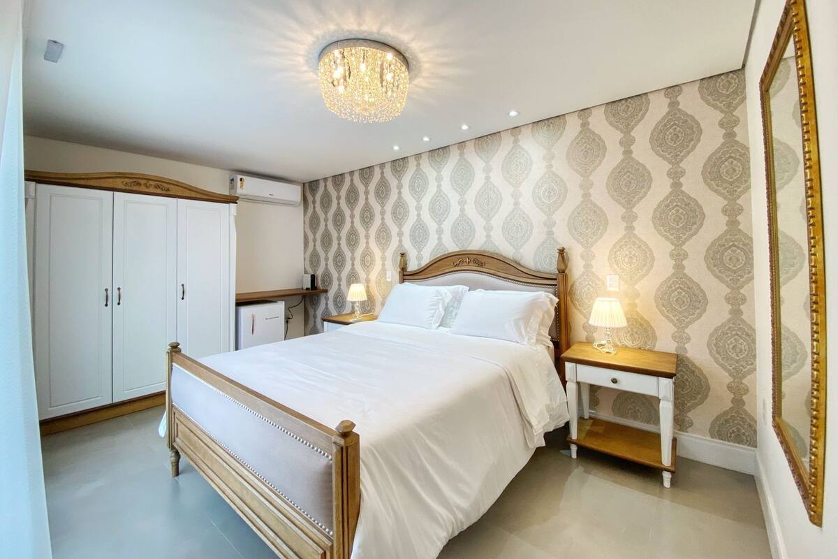 A bedroom with a large bed, a nightstand, a wardrobe, and a chandelier.