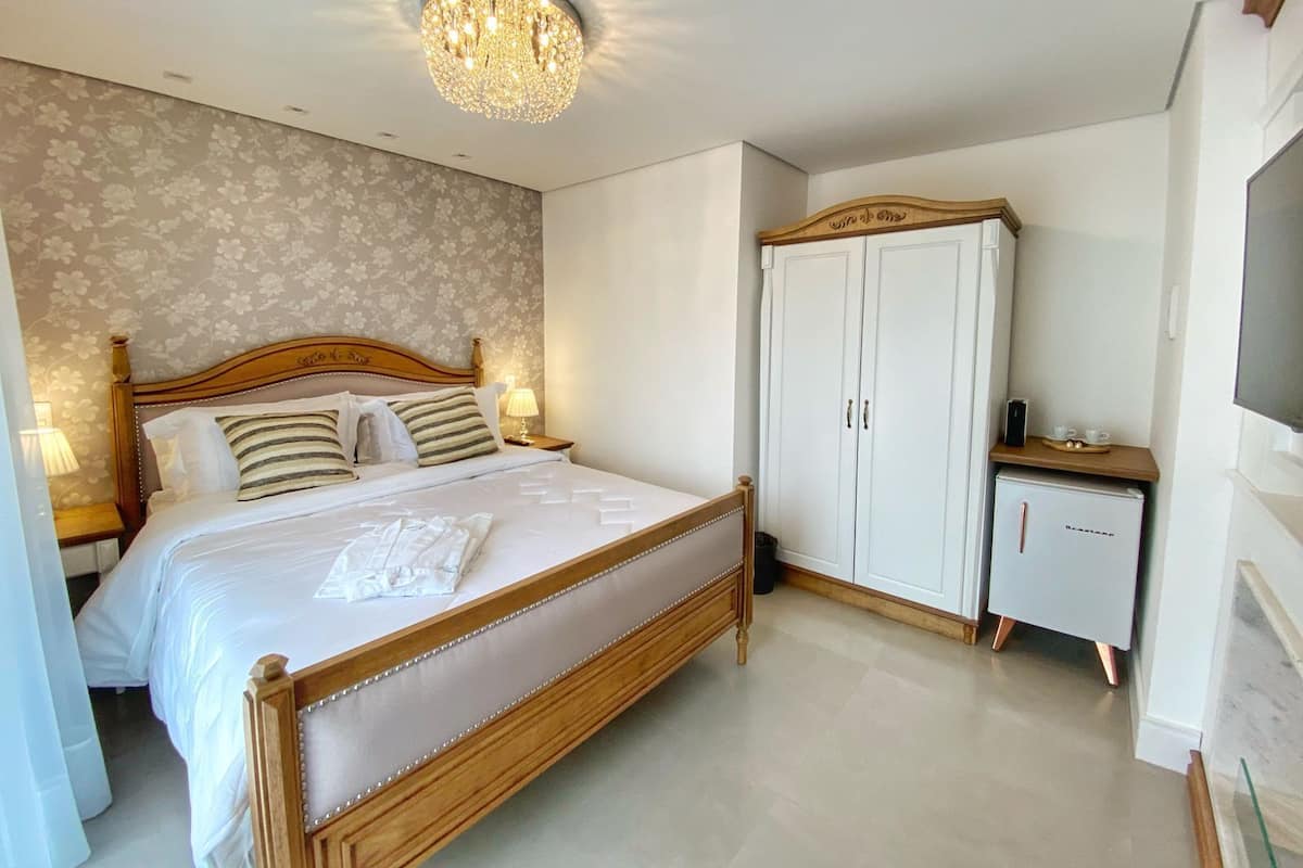 A bedroom with a large bed, a wardrobe, a small table with a TV, and a chandelier.
