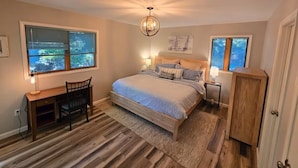 A bedroom with a bed, desk, chair, and a view of the outdoors through the windows. - Secluded 4BR Cottage Near Lake Michigan—Decks, Fire Pit & Pet‑Friendly (South Haven)