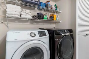 Ein Waschraum mit einer Samsung Waschmaschine und einem Trockner, Regalen mit gefalteten Handtüchern und Reinigungsmitteln.