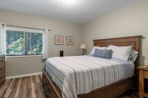 A bedroom with a wooden bed, a window with blinds, a bedside table, and a nightstand. - Secluded 4BR Cottage Near Lake Michigan—Decks, Fire Pit & Pet‑Friendly (South Haven)