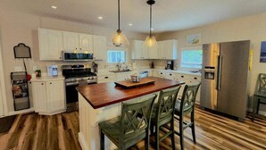 A modern kitchen with white cabinets, a wooden island with chairs, a stainless steel refrigerator, and pendant lighting. - Secluded 4BR Cottage Near Lake Michigan—Decks, Fire Pit & Pet‑Friendly (South Haven)
