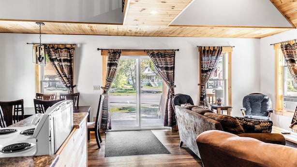 Un accogliente soggiorno con angolo cottura, soffitto in legno e ampie finestre con tende a motivi decorativi.