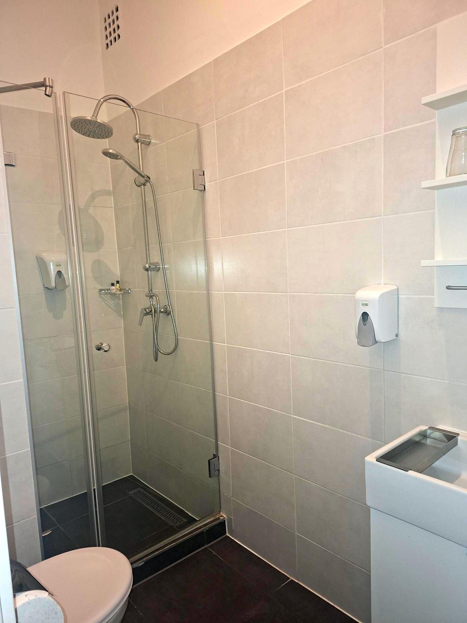 A modern bathroom with a glass-enclosed shower, a toilet, and a sink with a soap dispenser.